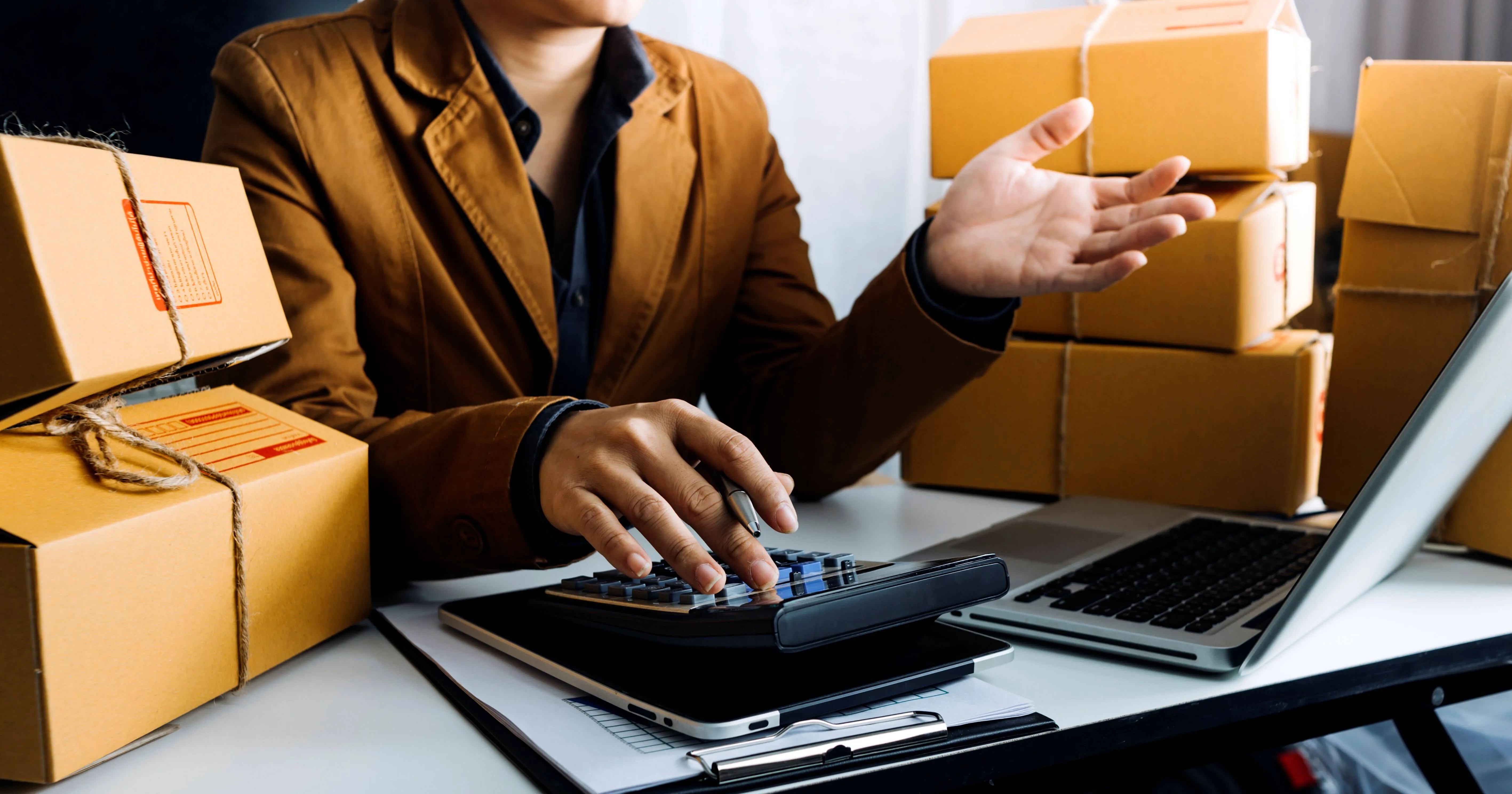 Asian man surrounded by boxes, answering phone calls about sales tax for drop shipping